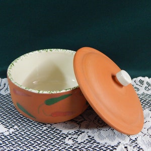 May include: Terracotta ceramic bowl with a lid, featuring a green and red chili pepper design. The bowl has a white interior and the lid has a white knob.