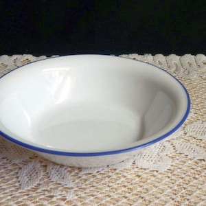 May include: A white ceramic bowl with a blue rim. The bowl is empty and sitting on a white lace tablecloth.