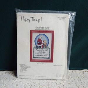 May include: Cross stitch kit featuring a Santa Claus kneeling with a child. The kit includes a counted design, Aida cloth, cotton floss, metallic thread, needle, and instructions. The text on the design reads "The perfect gift is not tied with a bow. It comes from the heart, through the love we show."