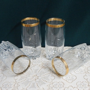 May include: Set of four clear glass drinking glasses with a gold rim. The glasses have a textured design.