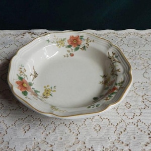 May include: A white ceramic soup bowl with a floral design featuring pink, yellow, and green flowers and birds. The bowl has a scalloped edge and a gold rim.