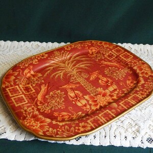 May include: Red and gold decorative serving tray with a rectangular shape and a gold trim. The tray features a detailed design of a palm tree, birds, and floral patterns. The tray is approximately 12 inches long and 8 inches wide.