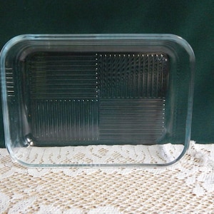 May include: A rectangular clear glass baking dish featuring a textured base with four distinct quadrants of alternating vertical and horizontal raised lines. The dish has rounded corners and smooth, transparent sides with a thick rim.