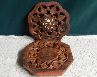 May include: A two-piece, wooden decorative item with intricate leaf carvings. The top piece is a floral design, and the bottom piece is a hexagonal shape. The center of the top piece has a circular inlay with a floral design.