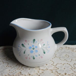 May include: White ceramic creamer with a blue rim and a floral design in pink, blue, and green.