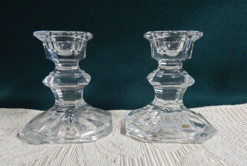 May include: A pair of clear glass candle holders with a faceted design. The candle holders are made by Mikasa.