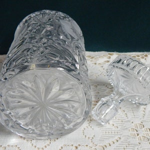 May include: A clear glass decanter with a stopper. The decanter has a cut glass design and is empty. The stopper is also cut glass and has a round top.