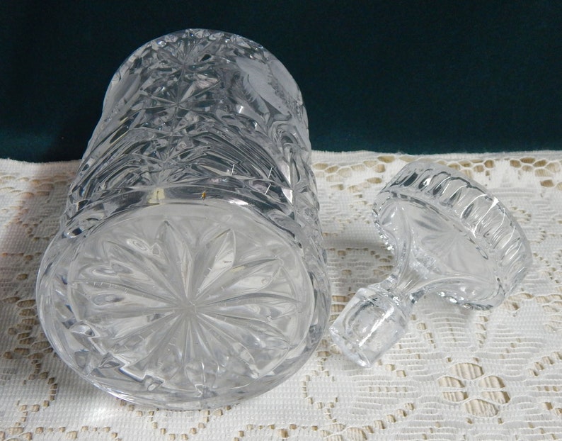 May include: A clear glass decanter with a stopper. The decanter has a cut glass design and is empty. The stopper is also cut glass and has a round top.