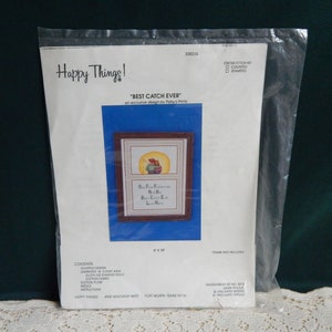 May include: A cross stitch kit featuring a design of two fishermen with the text "One Fine Fisherman And His Best Catch Ever -  La Here". The kit includes a chart, Aida cloth, cotton floss, needle, and instructions. The kit is 8 inches by 10 inches.