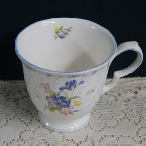 May include: A white ceramic mug with a blue rim and floral pattern. The mug has a handle and a pedestal base.