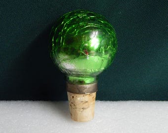 May include: Green glass bottle stopper with a cork base. The glass is textured and has a metallic sheen.