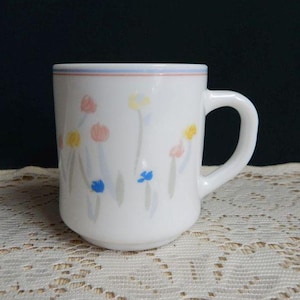 May include: White ceramic mug with a blue, red, and yellow floral design. The mug has a rounded handle.