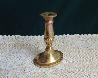 May include: A gold metal candlestick with a fluted design. The candlestick has a round base and a tall, slender stem.