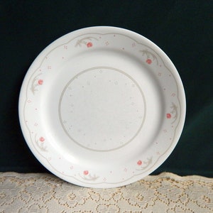 May include: A white ceramic dinner plate with a scalloped edge and a floral design in shades of pink and gray.