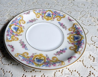 May include: A white porcelain saucer with a gold rim and a floral design. The design features pink, blue, and yellow flowers, as well as gold scrollwork.