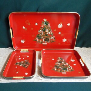May include: Set of three red and gold Christmas trays with a Christmas tree design and white snowflakes. The trays have woven handles.