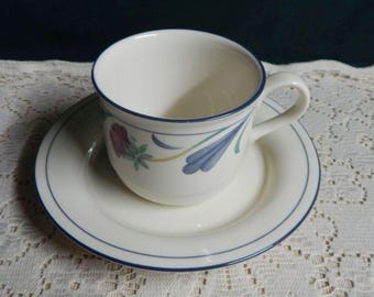 May include: A white teacup and saucer with a blue floral design. The cup has a blue rim and the saucer has a blue band around the edge.