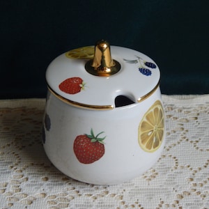 May include: White ceramic sugar bowl with a gold lid and rim. The bowl is decorated with a colorful fruit design featuring strawberries, lemons, and blackberries.