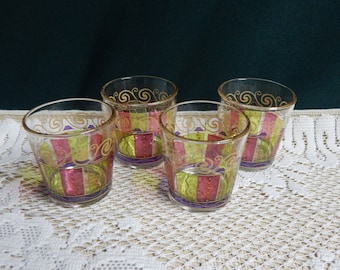 May include: Four clear glass tumblers with a decorative design. The glasses have a yellow, pink, and purple striped pattern with gold accents.