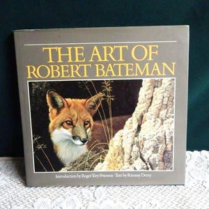 May include: The Art of Robert Bateman book cover featuring a painting of a red fox peering out from behind a tree trunk. The book title is in yellow text on a gray background.
