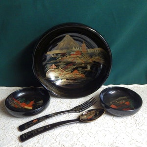 May include: A set of black lacquer bowls with gold and red painted designs. The bowls feature a Japanese landscape scene with a mountain, trees, and buildings. The set also includes a pair of chopsticks and a spoon.