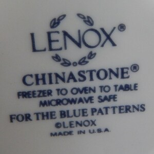 May include: Close-up of a white ceramic plate with blue text that reads "LENOX&reg; CHINASTONE&reg; FREEZER TO OVEN TO TABLE MICROWAVE SAFE FOR THE BLUE PATTERNS OLENOX MADE IN U.S.A."