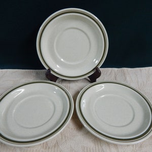 May include: Three white ceramic saucers with a green band around the edge. The saucers are for coffee or tea.