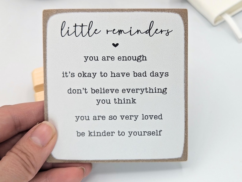 May include: A square wooden sign with a white face and brown edges. The text reads: little reminders, you are enough, it's okay to have bad days, don't believe everything you think, you are so very loved, be kinder to yourself.