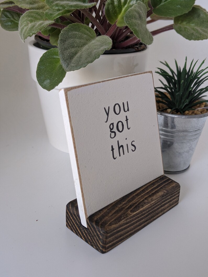 Może przedstawiać: Biały drewniany znak z napisem "you got this" czarnymi literami. Znak stoi na ciemnobrązowym drewnianym stojaku.