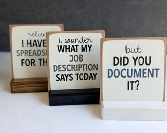 May include: Three rectangular signs with white faces and black text. The left sign reads "relax I HAVE SPREADSHEETS FOR THAT". The middle sign reads "i wonder WHAT MY JOB DESCRIPTION SAYS TODAY". The right sign reads "but DID YOU DOCUMENT IT?".
