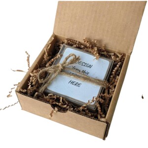 May include: A small cardboard box with a white card inside. The card has the text "DESIGN from this HERE" written on it. The box is filled with brown packing paper.