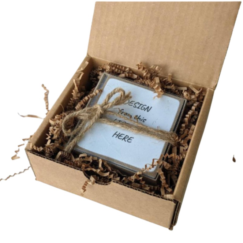 May include: A small cardboard box with a white card inside. The card has the text "DESIGN from this HERE" written on it. The box is filled with brown packing paper.