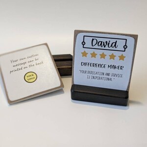 May include: A small, brown wooden plaque with a white background and gold stars. The plaque has the name "David" and the text "Difference Maker" with the quote "Your dedication and service is inspirational".