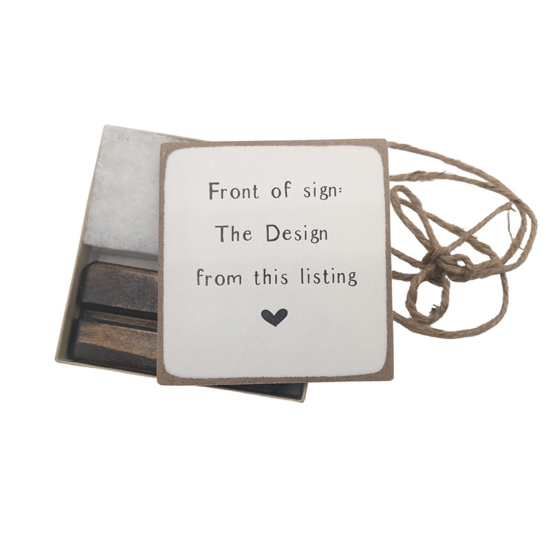 May include: A white sign with brown trim reads "Front of sign: The Design from this listing" with a small black heart below the text. The sign is in a box with a brown wooden stand and a piece of twine.
