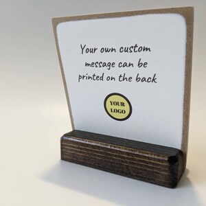 May include: A white card with a brown border sits on a dark brown wooden stand. The card has the text "Your own custom message can be printed on the back" and a yellow circle with the text "YOUR LOGO" in black.