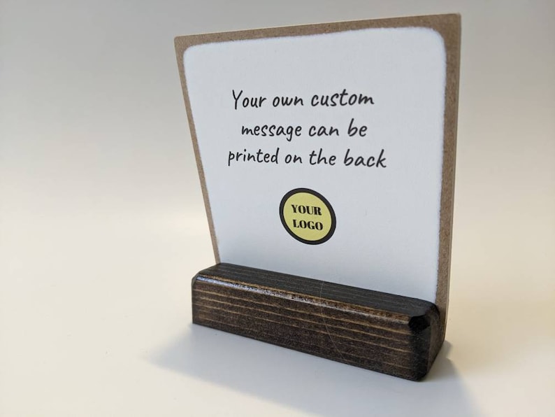 May include: A white card with a brown border sits on a dark brown wooden stand. The card has the text "Your own custom message can be printed on the back" and a yellow circle with the text "YOUR LOGO" in black.