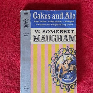 May include: Vintage paperback book titled "Cakes and Ale" by W. Somerset Maugham. The cover features a blue banner with the title, a portrait, and pink and yellow vertical stripes. The book is a Pocket Book edition.