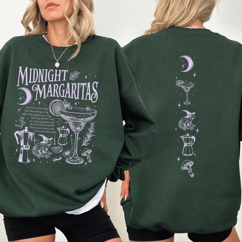 May include: Dark green sweatshirt featuring the text "Midnight Margaritas" and a cocktail illustration. The front design includes a moon, cocktail glass, and other graphics. The back features a moon, cocktail, frog, coffee pot, and mushroom.