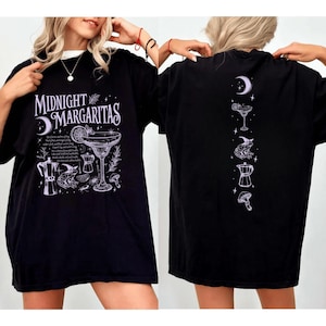 May include: Black t-shirt with the text "Midnight Margaritas" and a cocktail graphic on the front. The back of the shirt features a series of cocktail-themed illustrations. The shirt is a casual, oversized fit.