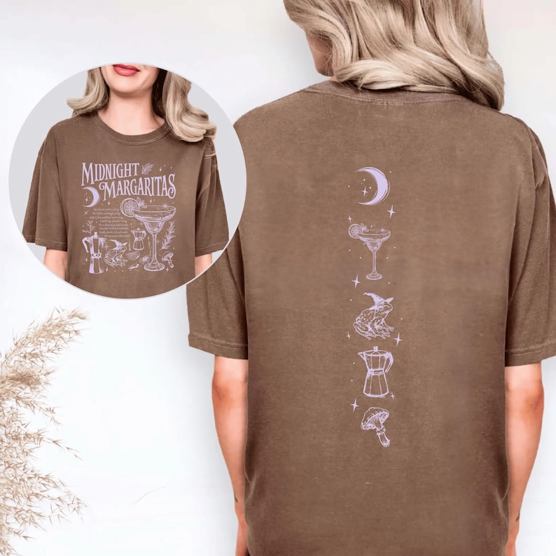 May include: Brown t-shirt featuring the text "Midnight Margaritas" and a cocktail illustration on the front. The back displays a vertical design with a crescent moon, cocktail, frog, coffee pot, and mushroom.