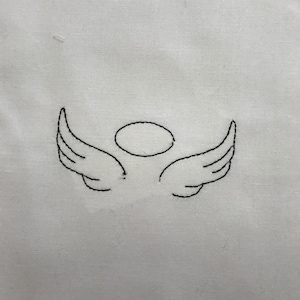 May include: A simple black line drawing of a pair of angel wings with a halo above them, stitched onto a white fabric background.