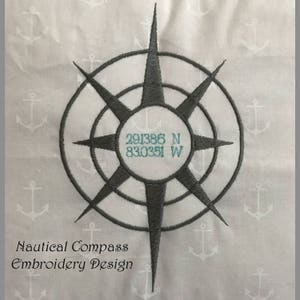 Puede incluir: Diseño de brújula náutica bordada en gris, con un círculo central con coordenadas y un patrón de estrella. El fondo es blanco con un patrón de anclas repetidas. El texto en la parte inferior dice "Nautical Compass Embroidery Design."