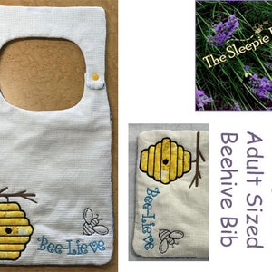 May include: White bib with a beehive and bee embroidery. The bib has a large opening for the head and two yellow buttons on the shoulders. The text "Bee-Lieve" is embroidered on the bib.