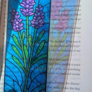 May include: A rectangular bookmark featuring a stained-glass design of lavender flowers with purple blooms and green stems against a blue background. The bookmark is held next to a book, with the text "Everlight" visible.
