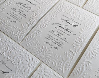 May include: A white wedding invitation with an embossed floral design. The invitation reads "Join us in a celebration of love as Annabele & Johnathan are getting married Saturday, 24 August 2024, 3 o'clock in the afternoon, Valle de Guadalupe, Baja California, Mexico."