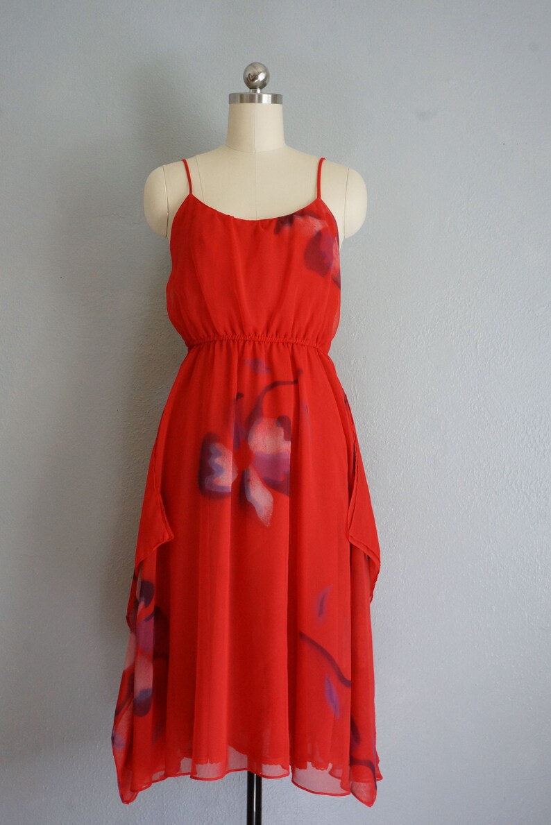 May include: A red sleeveless dress with a floral print. The dress has a gathered waist and a flowing skirt.