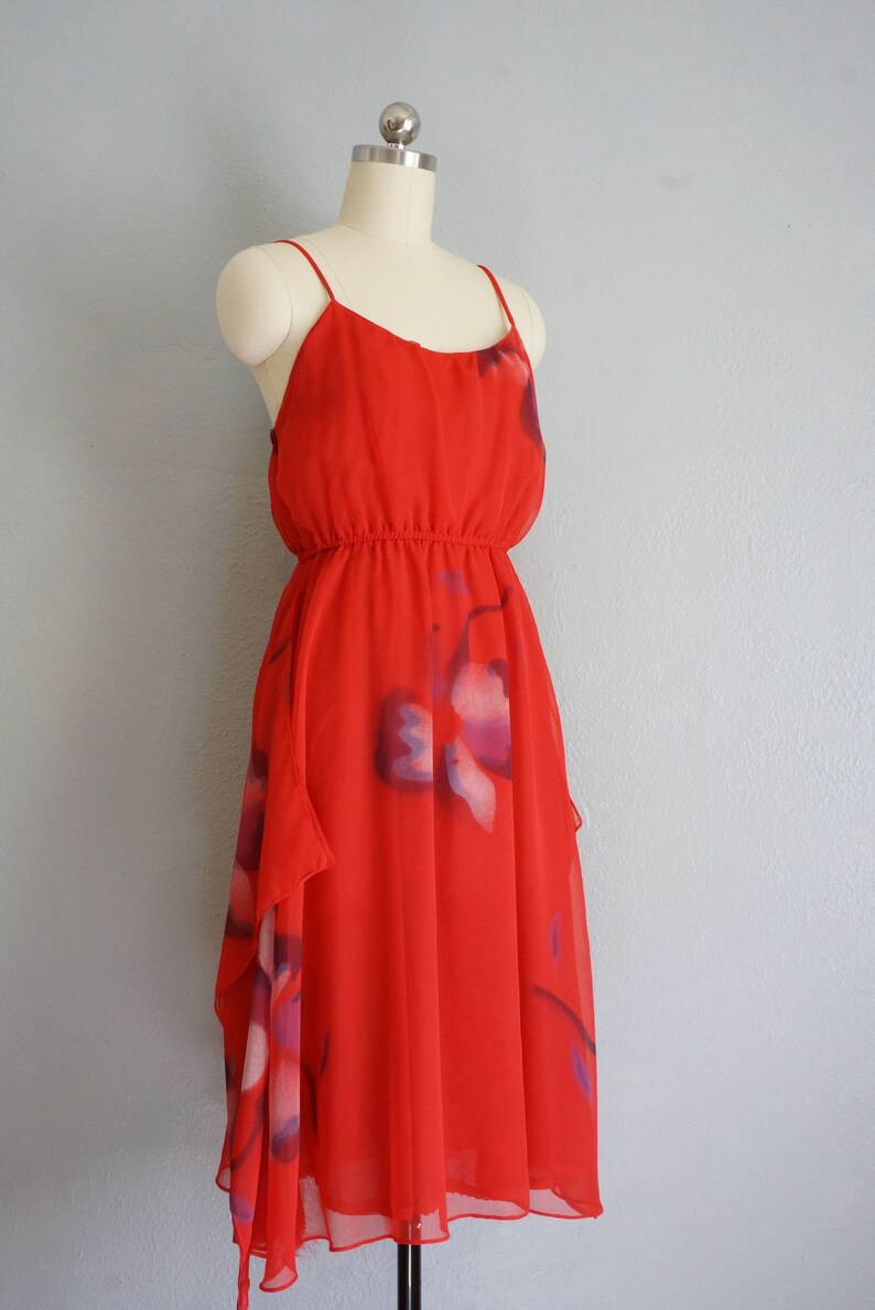 May include: A red sleeveless dress with a floral print. The dress has a fitted bodice and a flowing skirt.
