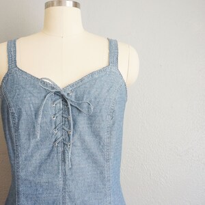 May include: A light blue denim dress with a lace-up front and thin straps. The dress is on a white mannequin.