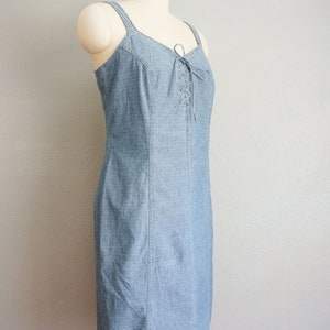 May include: A light blue denim dress with a lace-up detail at the bodice. The dress has a fitted silhouette and a straight hemline.