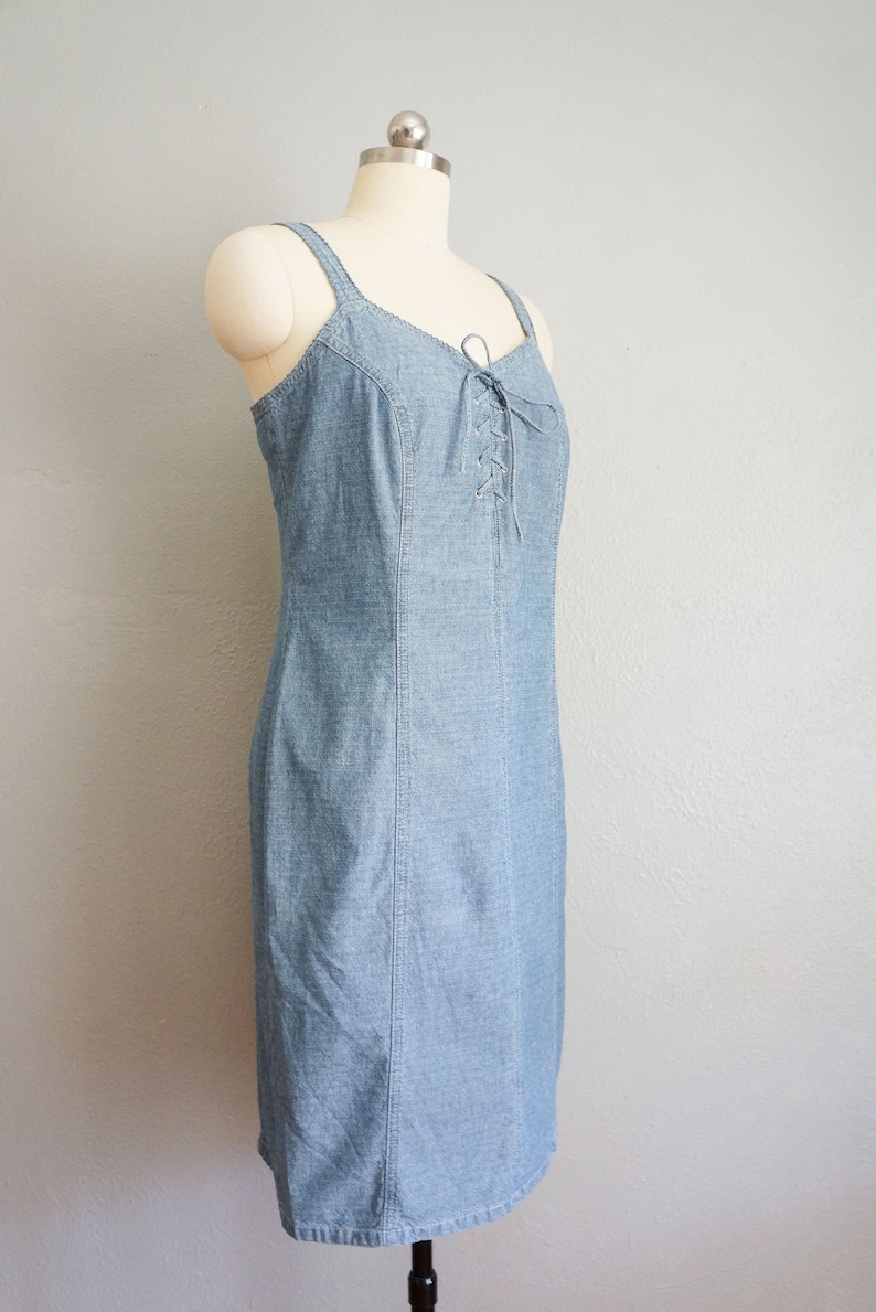 May include: A light blue denim dress with a lace-up detail at the bodice. The dress has a fitted silhouette and a straight hemline.